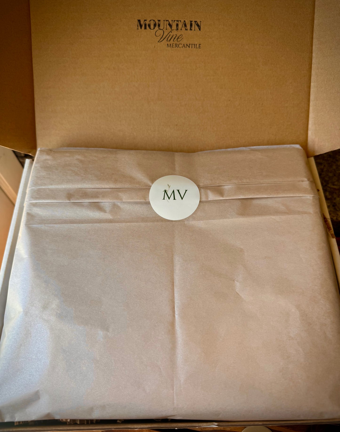 Open Mountain Vine Mercantile gift box showing the champagne colored wrapping tissue and MV logo sticker.
