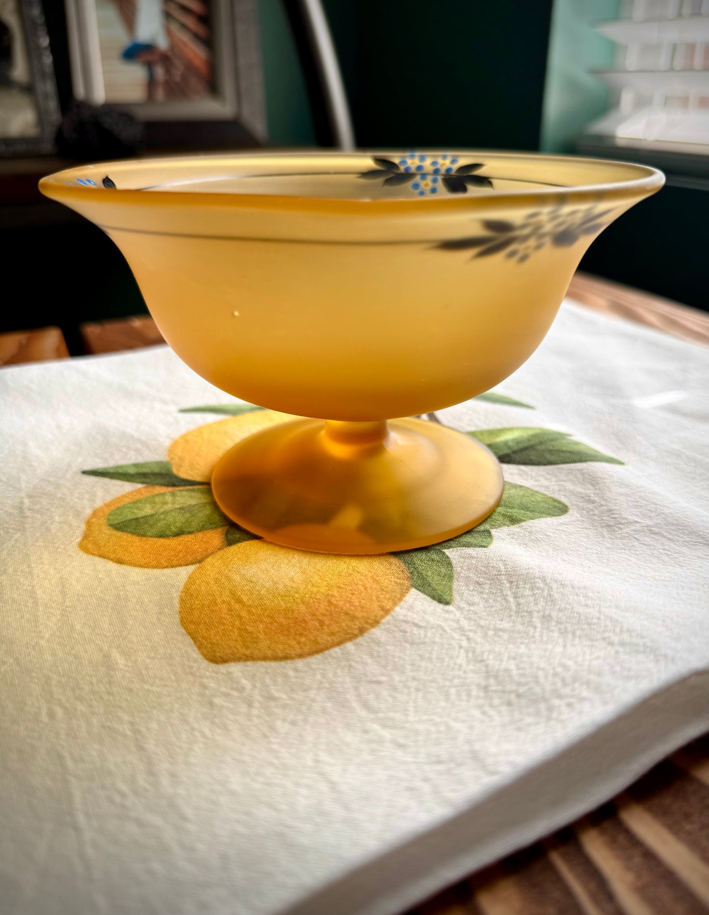 A close up side view of a frosted yellow vintage compote with hand painted dainty blue flowers.