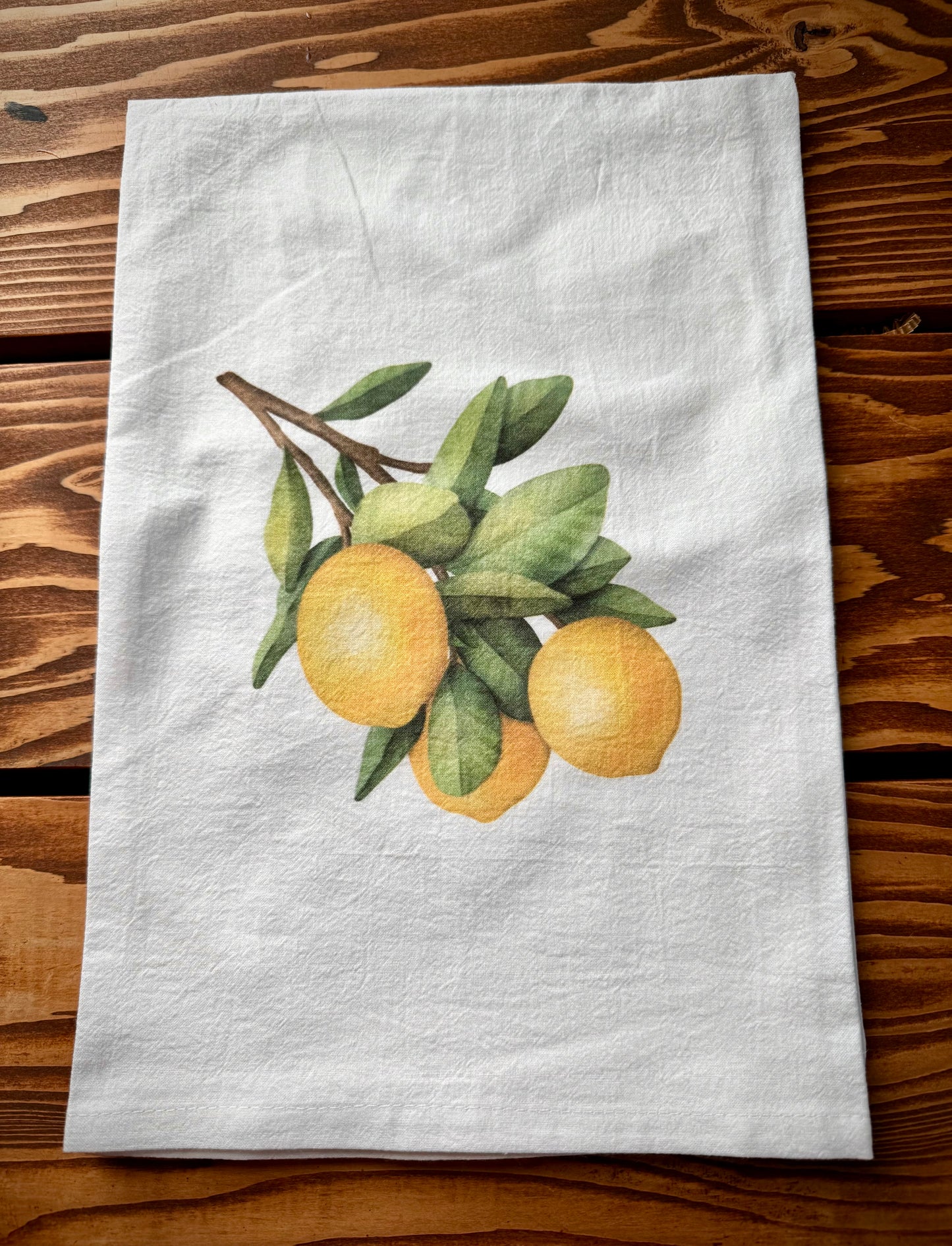 Close up of a white cotton flour sack tea towel with lemon branch print on top of wood background