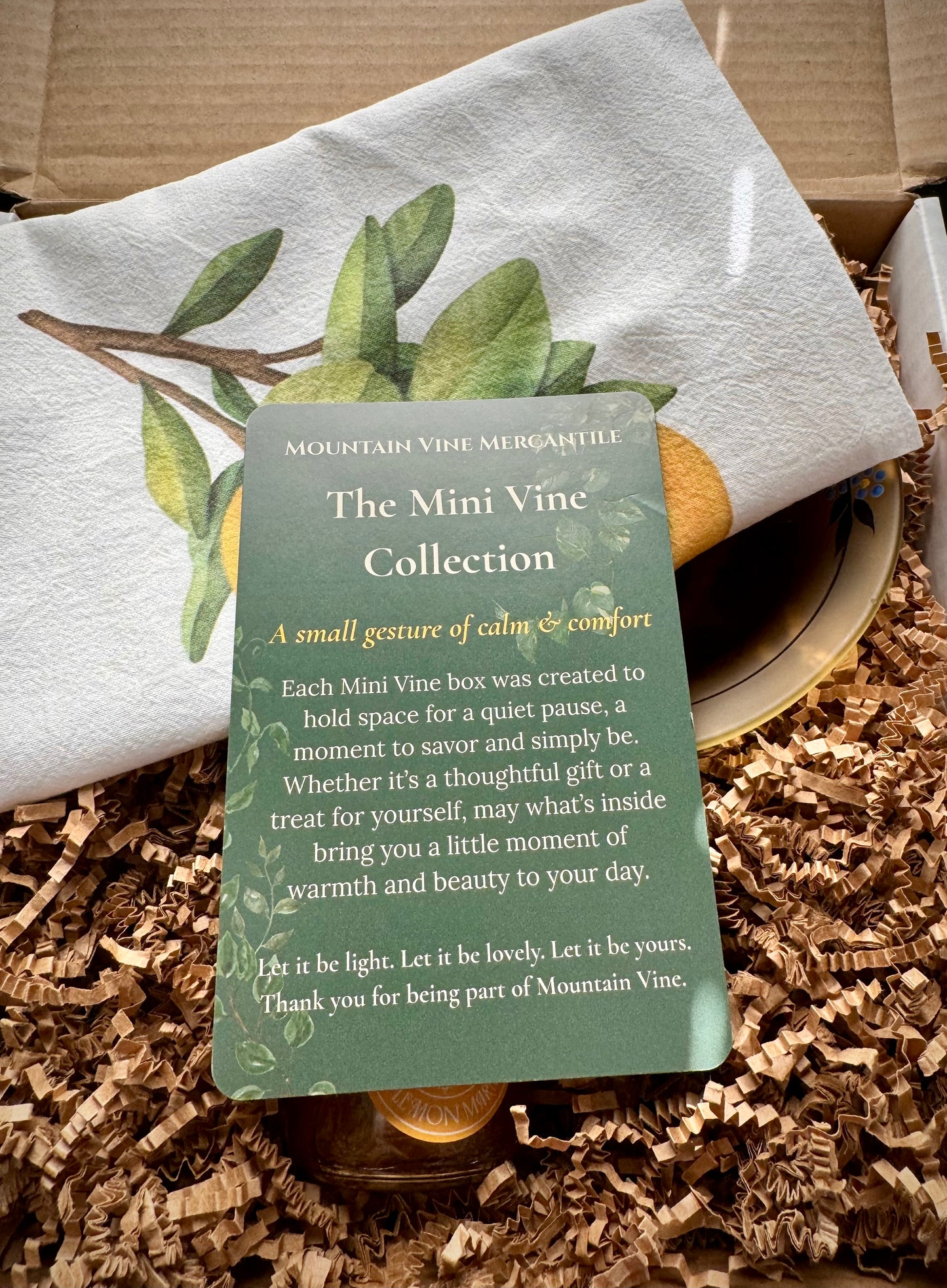 A green Mini Vine Collection product insert card on top of a white lemon branch tea towel and brown crinkle paper