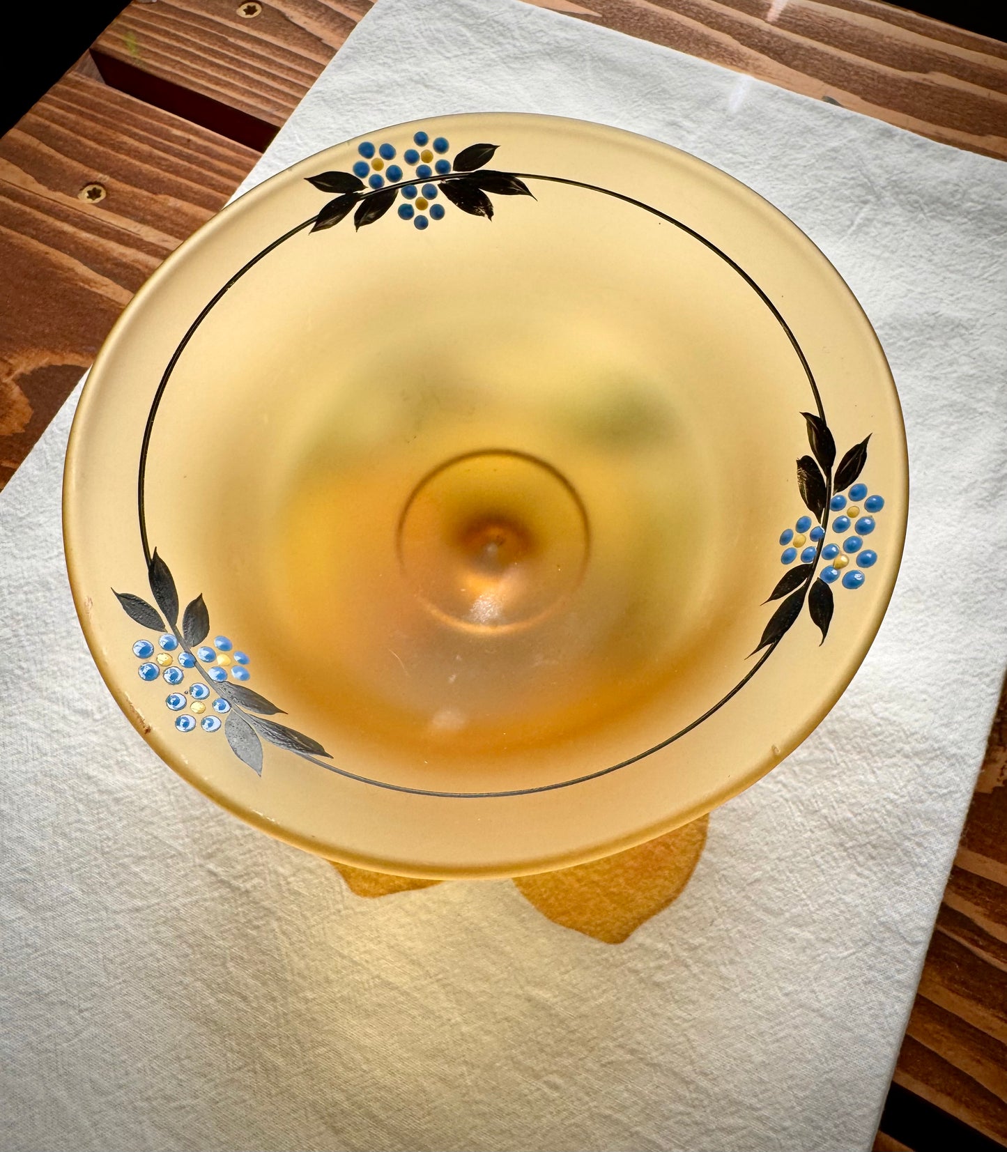 top down view of a vintage frosted yellow glass compte with dainty blue flowers on top of a white tea towel on a wood surface