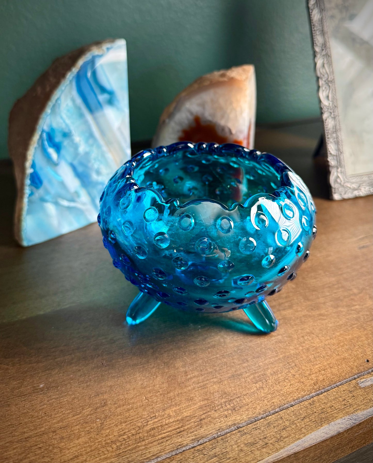 Vintage blue hobnail glass footed bowl on wood shelf with stones in the background. 