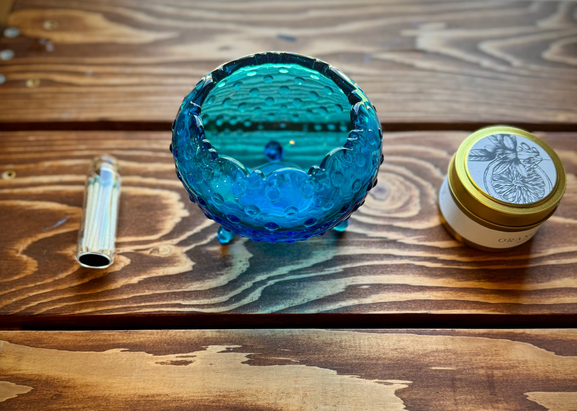 Close up detail shot of blue hobnail glass dish, match vial with green tipped matches and a botanical soy candle