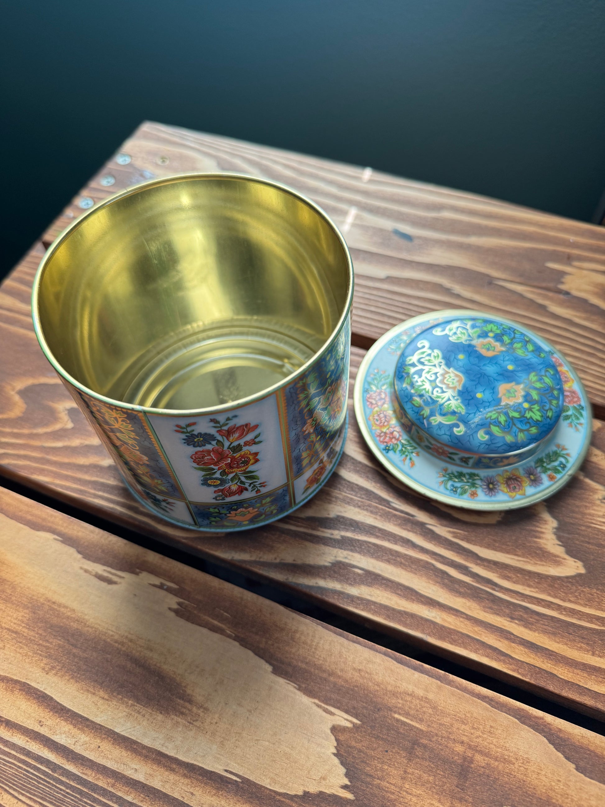 Top down view of vintage floral tea tin with the tin off and gold inside visible on a wood surface