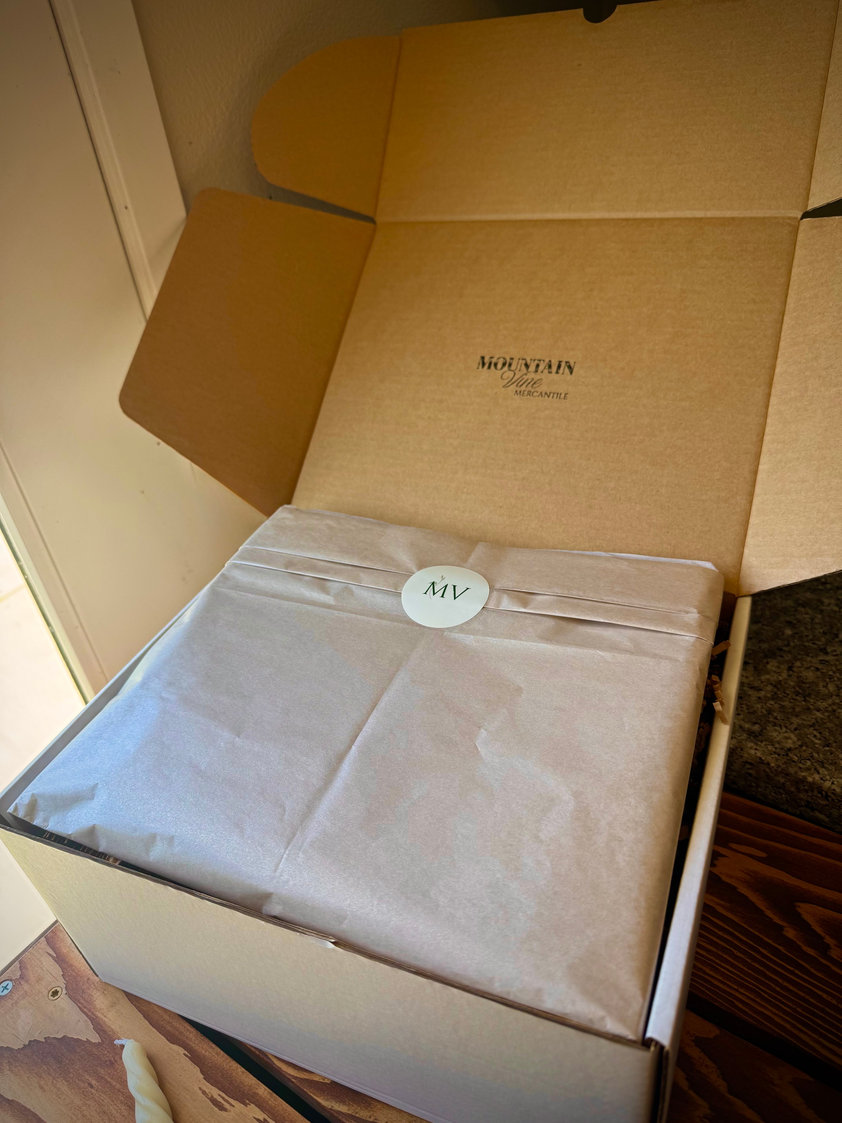 Mountain Vine Mercantile gift box open with the logo printed on the inside of lid. Champagne tissue paper folded over internal components with MV logo sticker centered. 