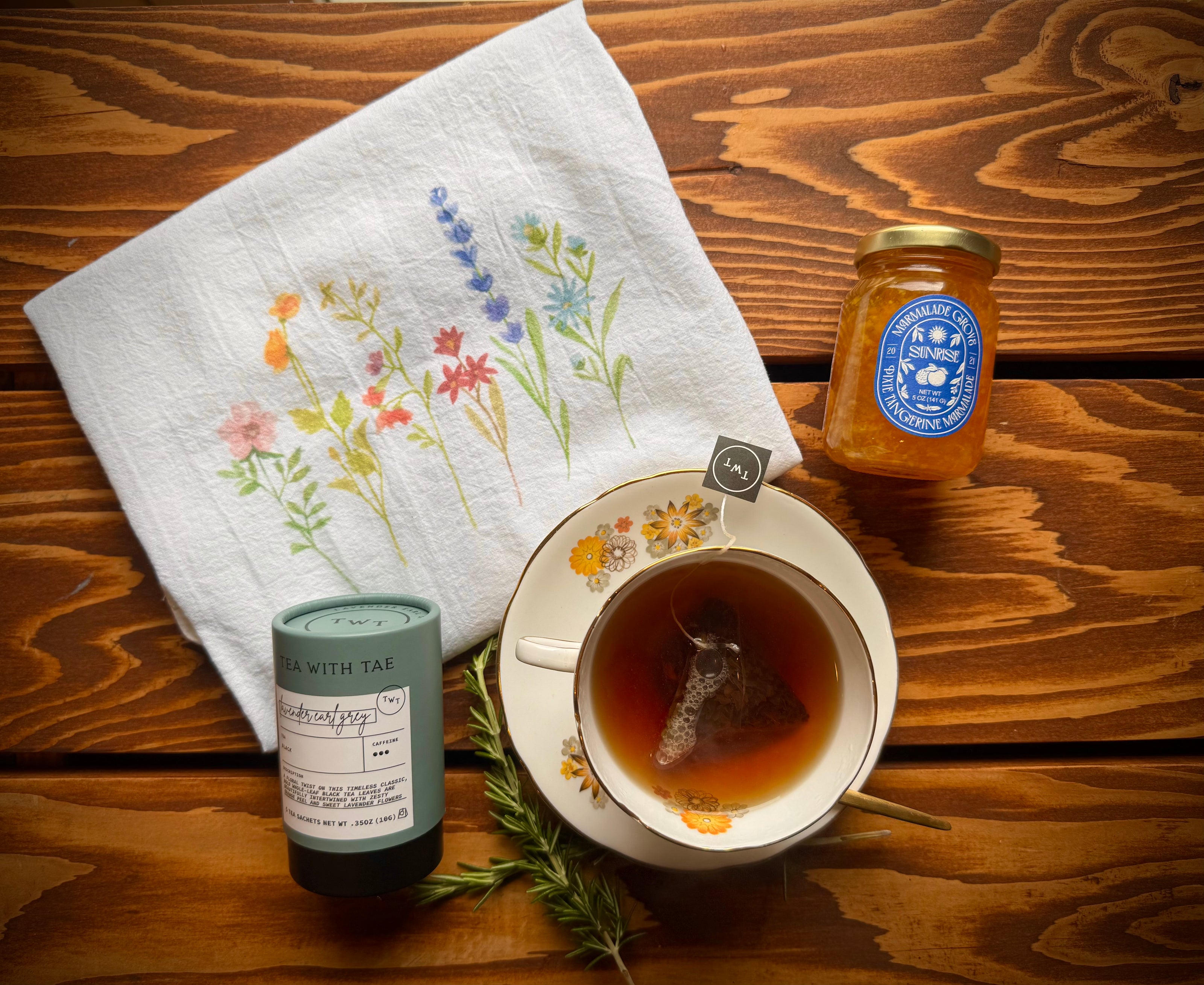 Mountain Morning Gift Box items from Mountain Vine Mercantile featuring Tea with Tae lavender Earl grey tea, tangerine marmalade, vintage floral teacup, wildflower tea towel and rosemary spring on rustic wood table