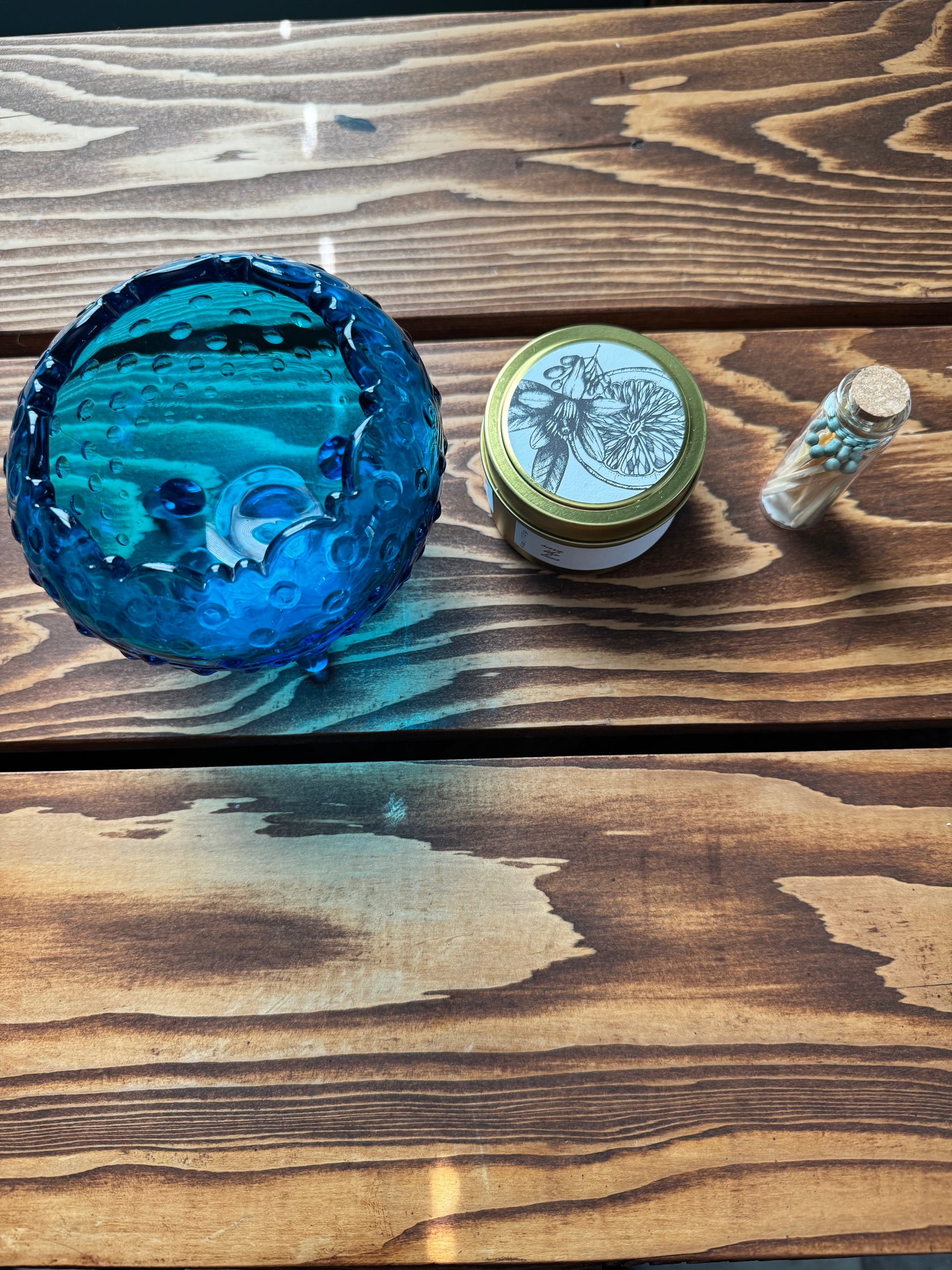 Blue hobnail vintage glass dish with soy candle and match vial in a row on a wood background
