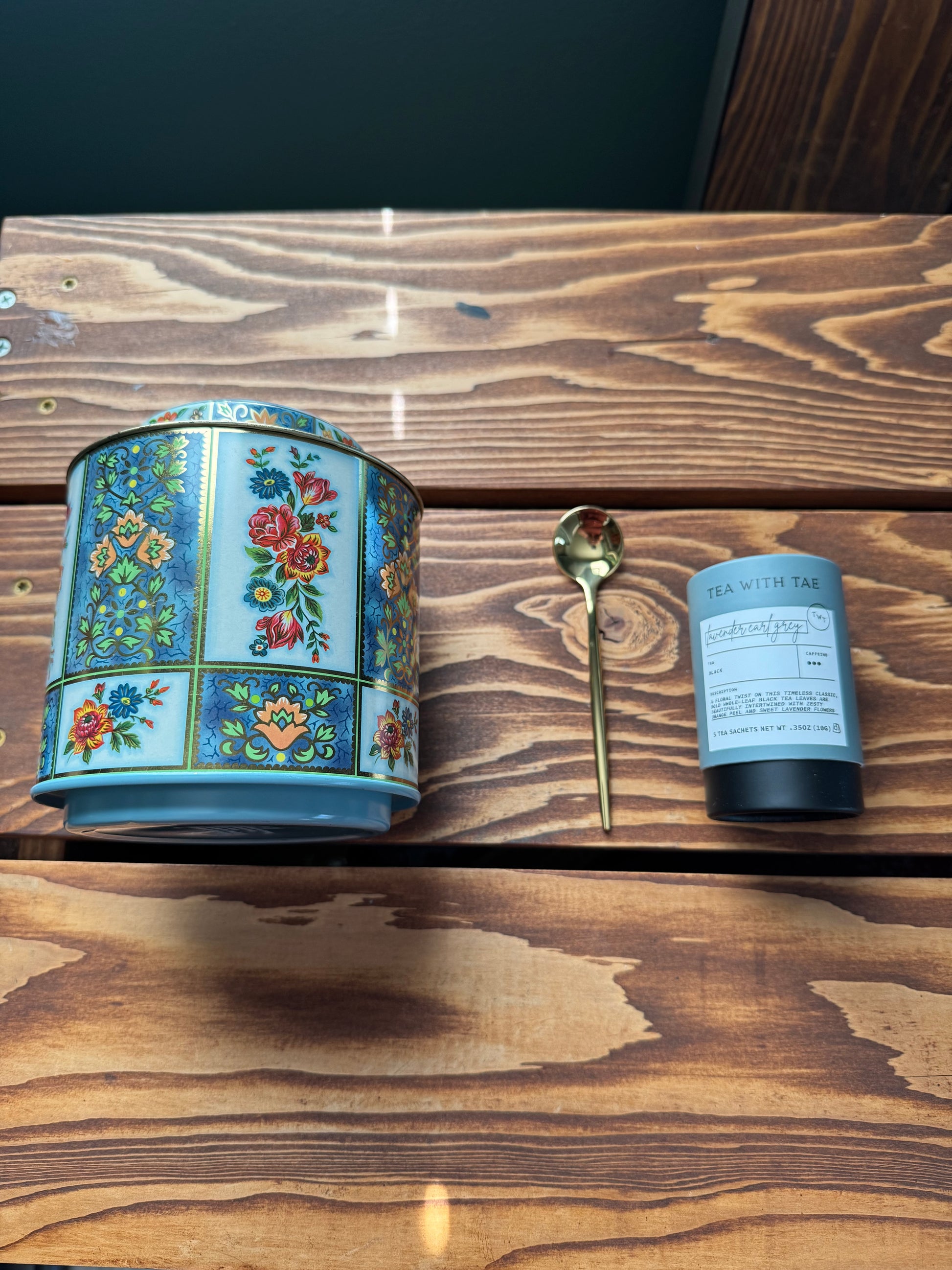 Flat Lay of a large blue floral English tea tin, gold teaspoon and tea with tae lavender Earl grey tea on a wood background